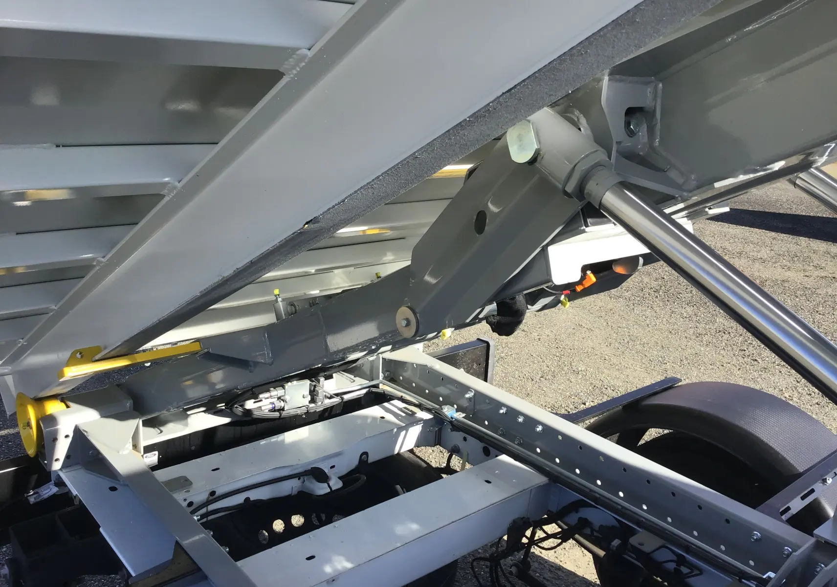 Gros plan sous la benne relevée du Ford Transit Chassis Cabine blanc, montrant le bras de levage et le châssis métallique.