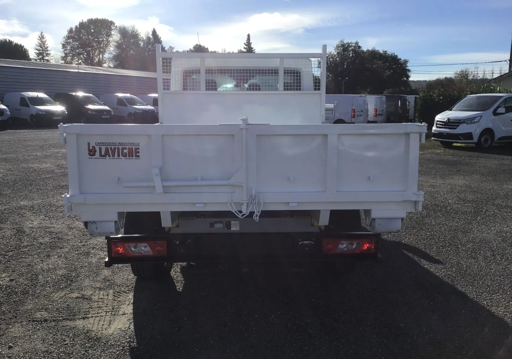 Vue arrière d'un Ford Transit Chassis Cabine blanc avec benne 3m20 et portes battantes, en extérieur.