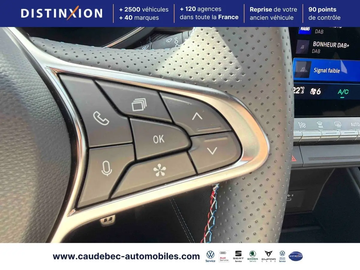 Gros plan sur les commandes multifonctions du volant perforé noir du Renault Symbioz gris, avec écran tactile en arrière-plan.