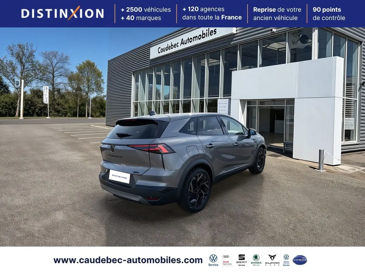 Vue 3/4 arrière droite d’un Renault Symbioz gris métallisé avec jantes noires devant un bâtiment de concession.