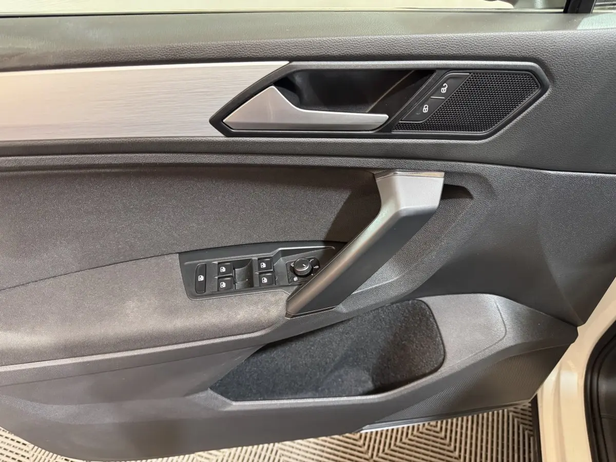 Vue intérieure côté gauche de la porte avant d'un Volkswagen Tiguan blanc avec commandes de vitres et verrouillage.