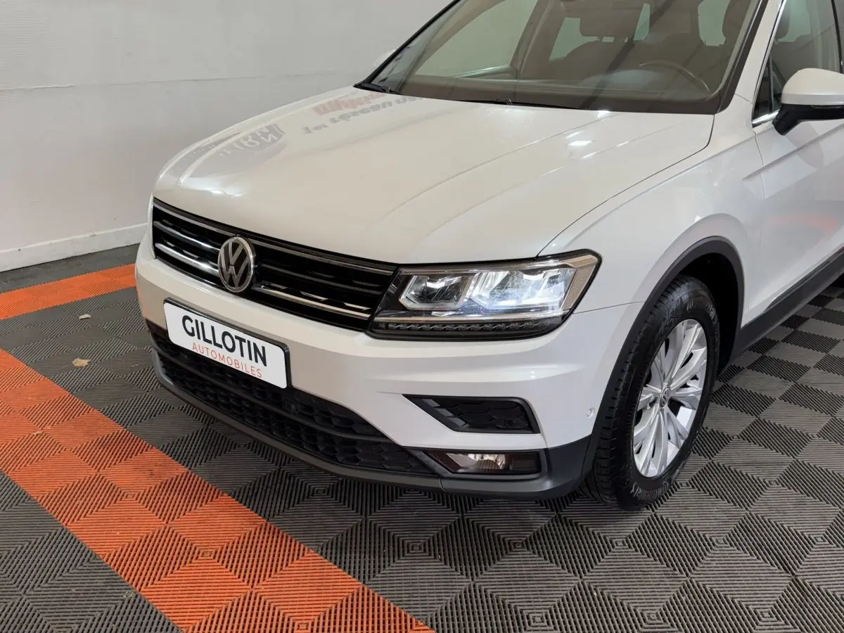 Vue 3/4 avant droit d'un Volkswagen Tiguan blanc avec phares LED allumés et jantes alliage.