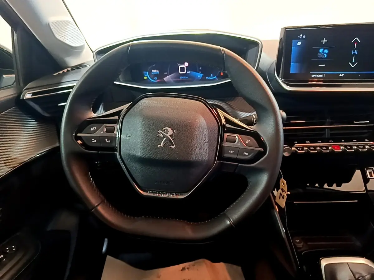 Vue intérieure centrée sur le volant cuir multifonctions de la Peugeot 208, avec tableau de bord digital et écran tactile.