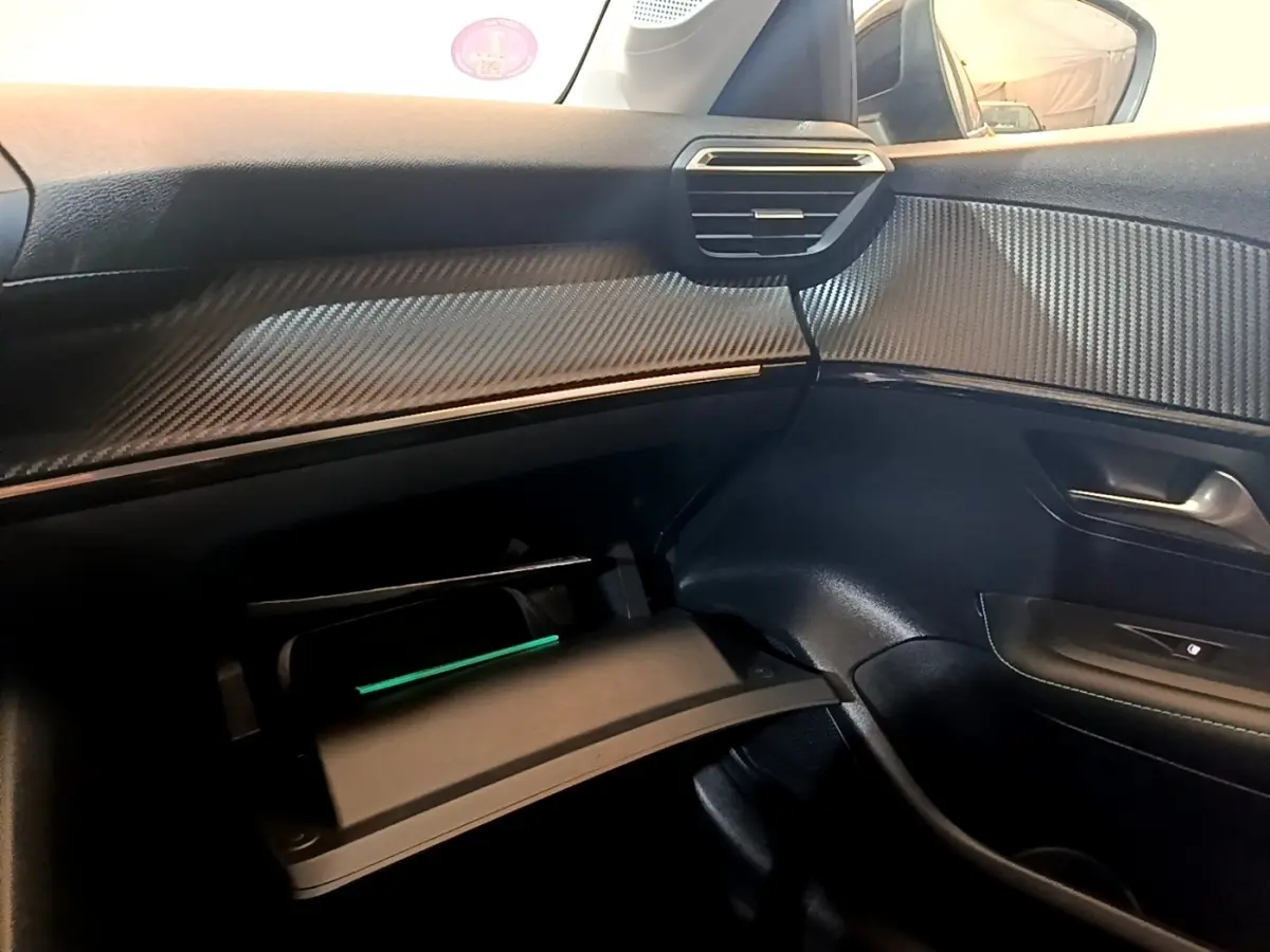 Vue intérieure côté passager du tableau de bord noir avec insert effet carbone et boîte à gants ouverte du Peugeot 208 jaune.