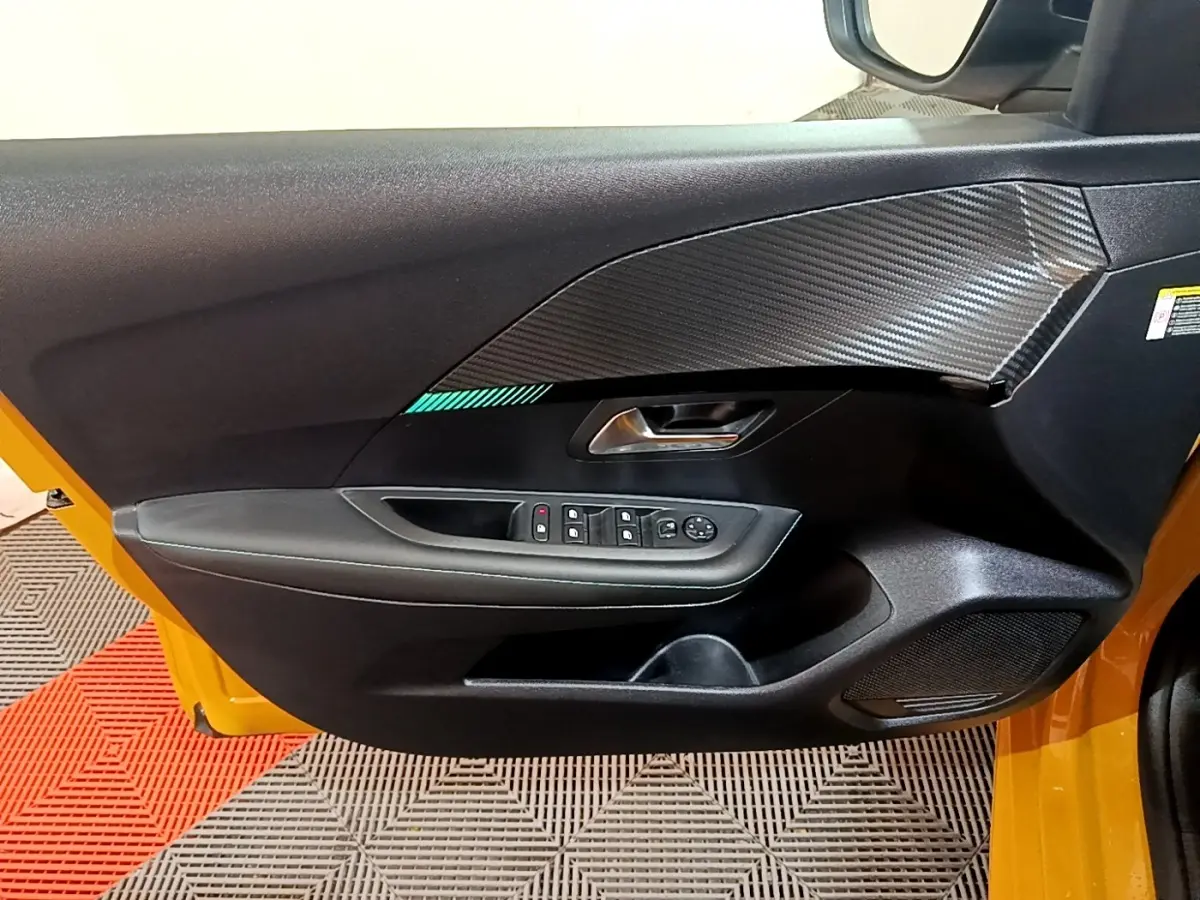 Vue intérieure de la porte avant gauche jaune de la Peugeot 208 2023 avec commandes électriques et insert décor carbone.