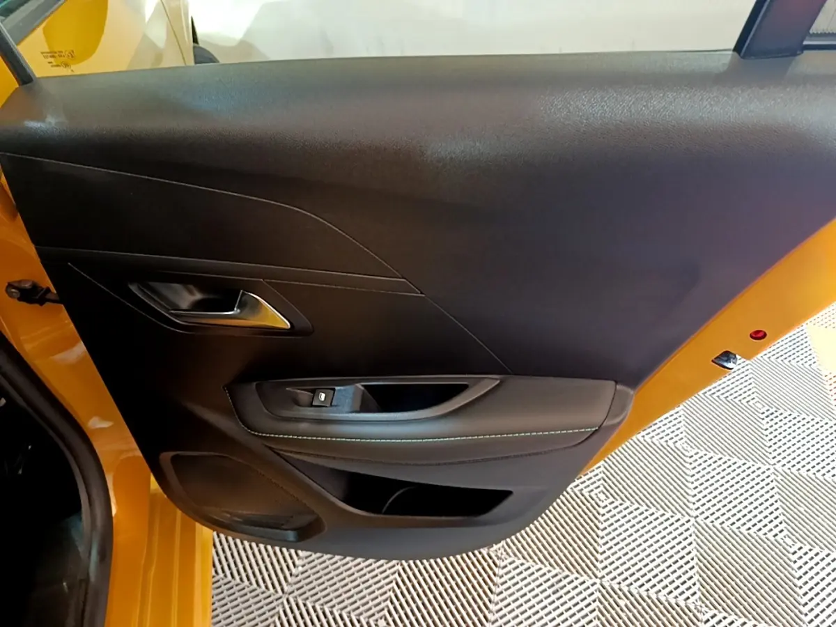 Vue rapprochée de la porte arrière gauche noire avec surpiqûres, sur Peugeot 208 jaune 2023.