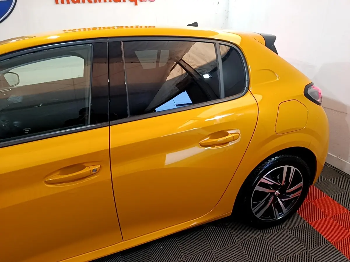 Vue côté droit arrière d'une Peugeot 208 jaune vif avec jante alliage et vitres teintées dans un intérieur showroom.