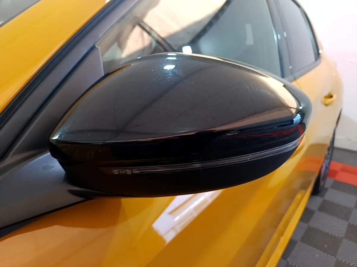 Rétroviseur noir côté gauche en gros plan sur Peugeot 208 jaune vue partielle avant.