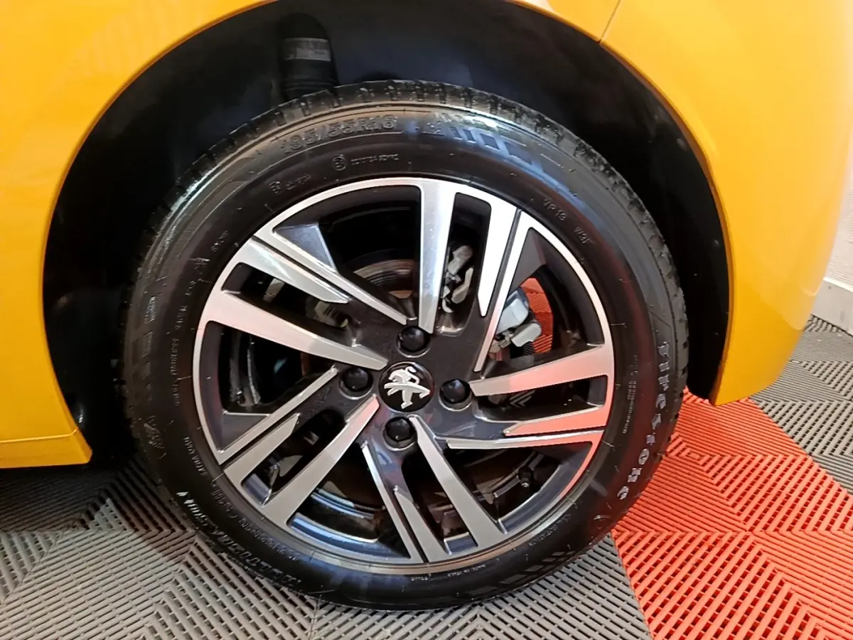 Gros plan sur la roue avant droite d'une Peugeot 208 jaune 2023 avec jante alliage noire et argentée.