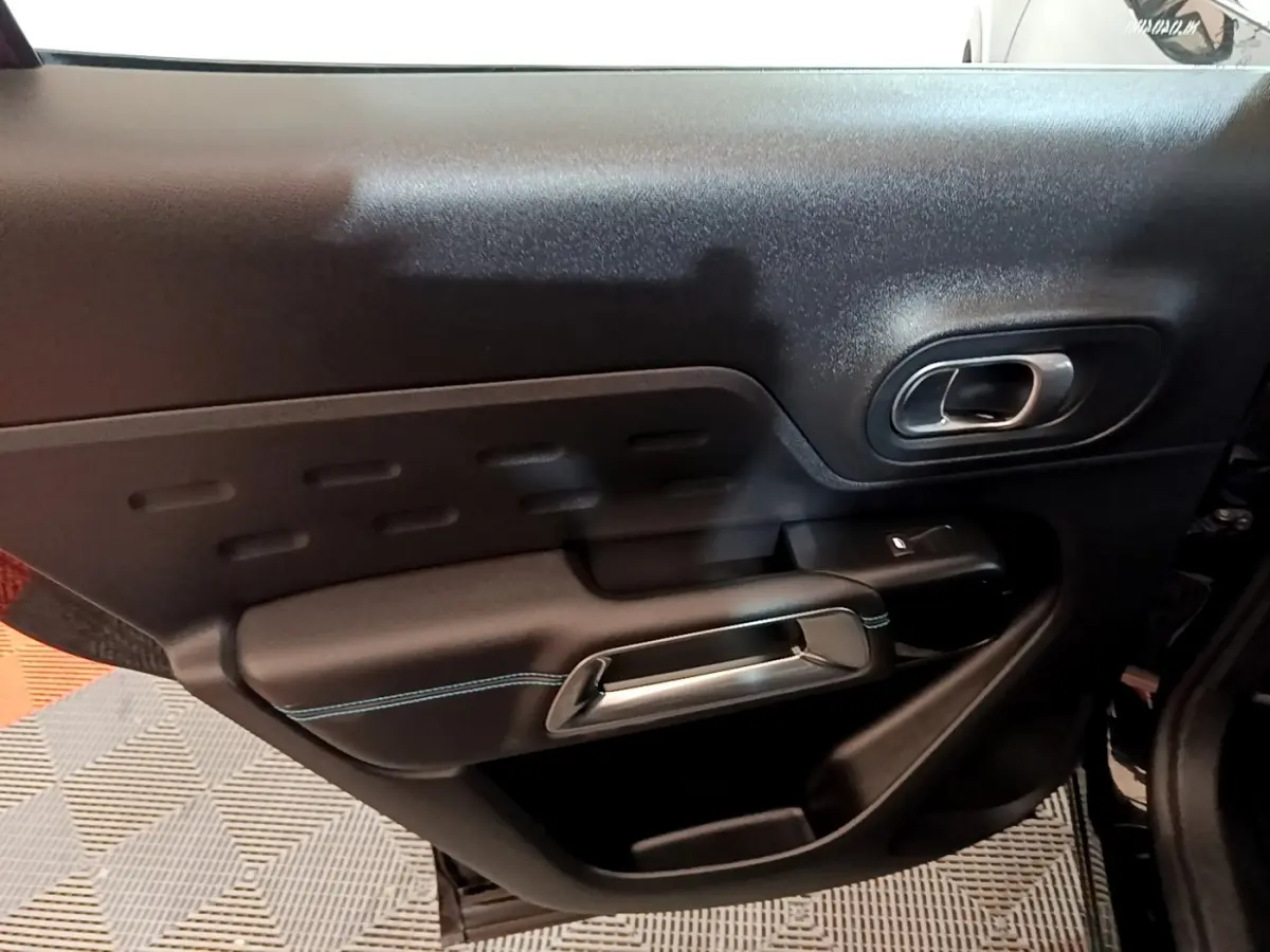 Gros plan sur la porte intérieure côté droit du Citroën C5 Aircross hybride noire, avec poignée argentée et surpiqûres bleues.