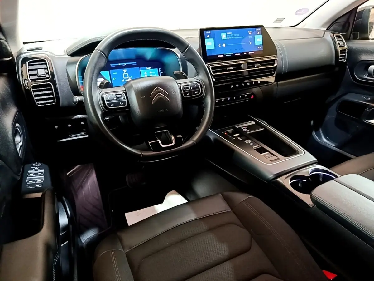 Intérieur noir du Citroën C5 Aircross hybride, vue avant centrée sur le volant multifonctions et l’écran tactile central.