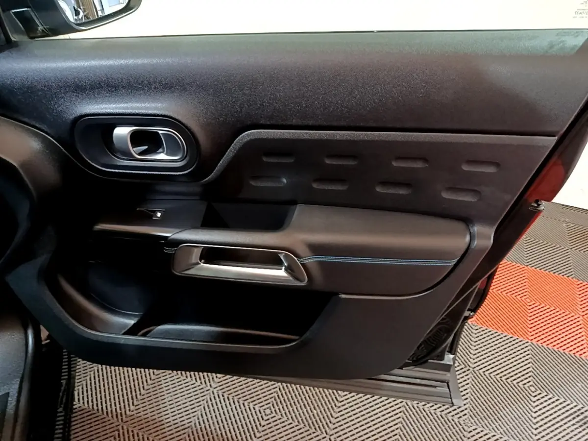 Gros plan sur la porte intérieure côté gauche du Citroën C5 Aircross hybride rechargeable 2022, avec poignée argentée et surpiqûres bleues.