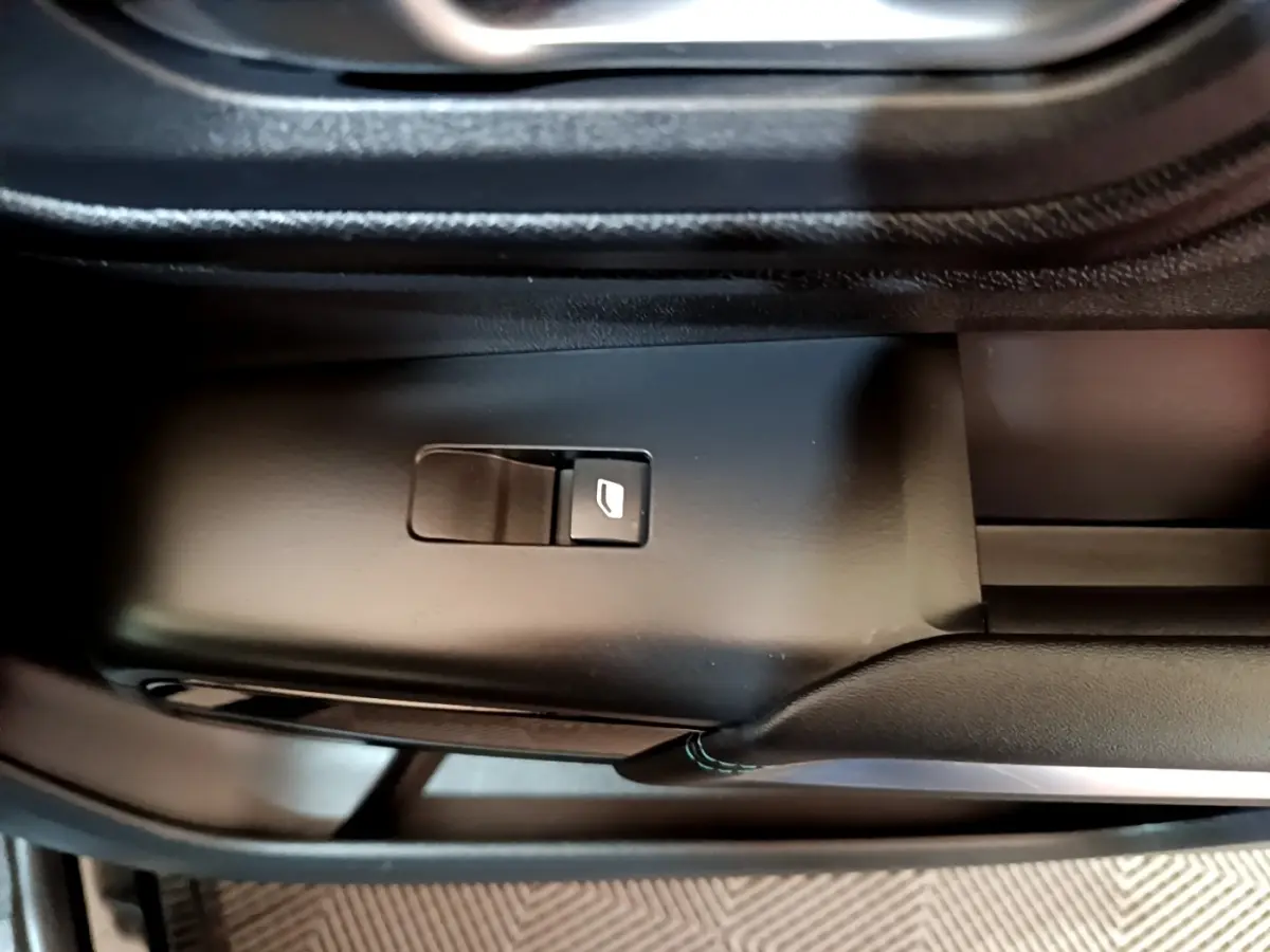 Gros plan sur le bouton de commande de la vitre électrique côté conducteur dans l'habitacle noir du Citroën C5 Aircross hybride.