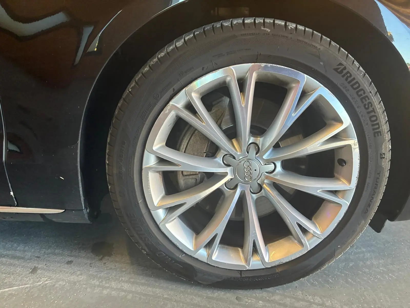 Gros plan sur la roue avant droite d'une Audi A8 noire 2016, avec jante alliage argentée à multiples branches fines.