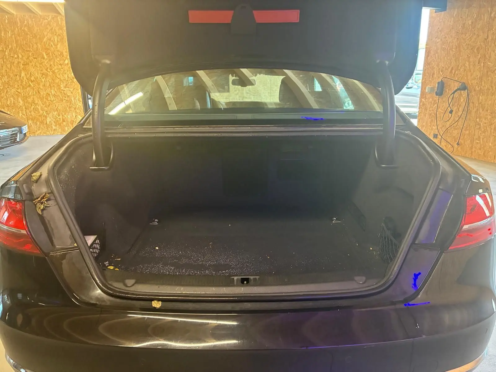 Vue arrière d’un coffre ouvert d’Audi A8 noire 2016, montrant l’espace de rangement vide et les feux arrière allumés.