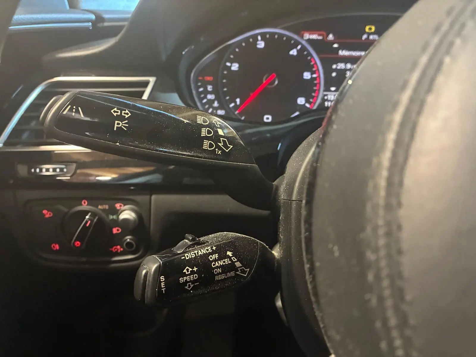 Gros plan sur les commandes au volant noir d'une Audi A8 2016, avec tableau de bord digital en arrière-plan.