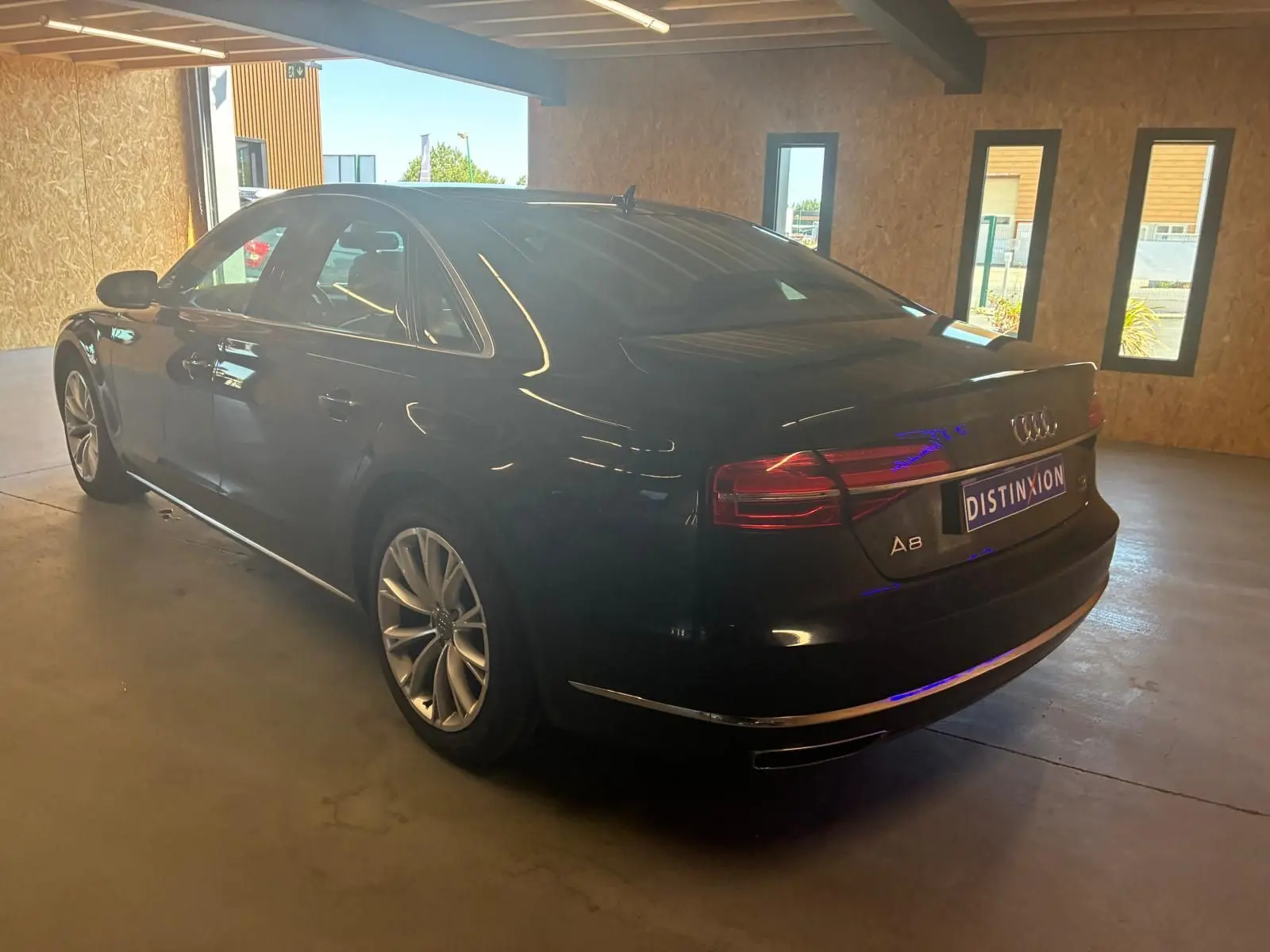Audi A8 noir vue en 3/4 arrière droit dans un garage, avec feux arrière allumés et jantes alliage visibles.