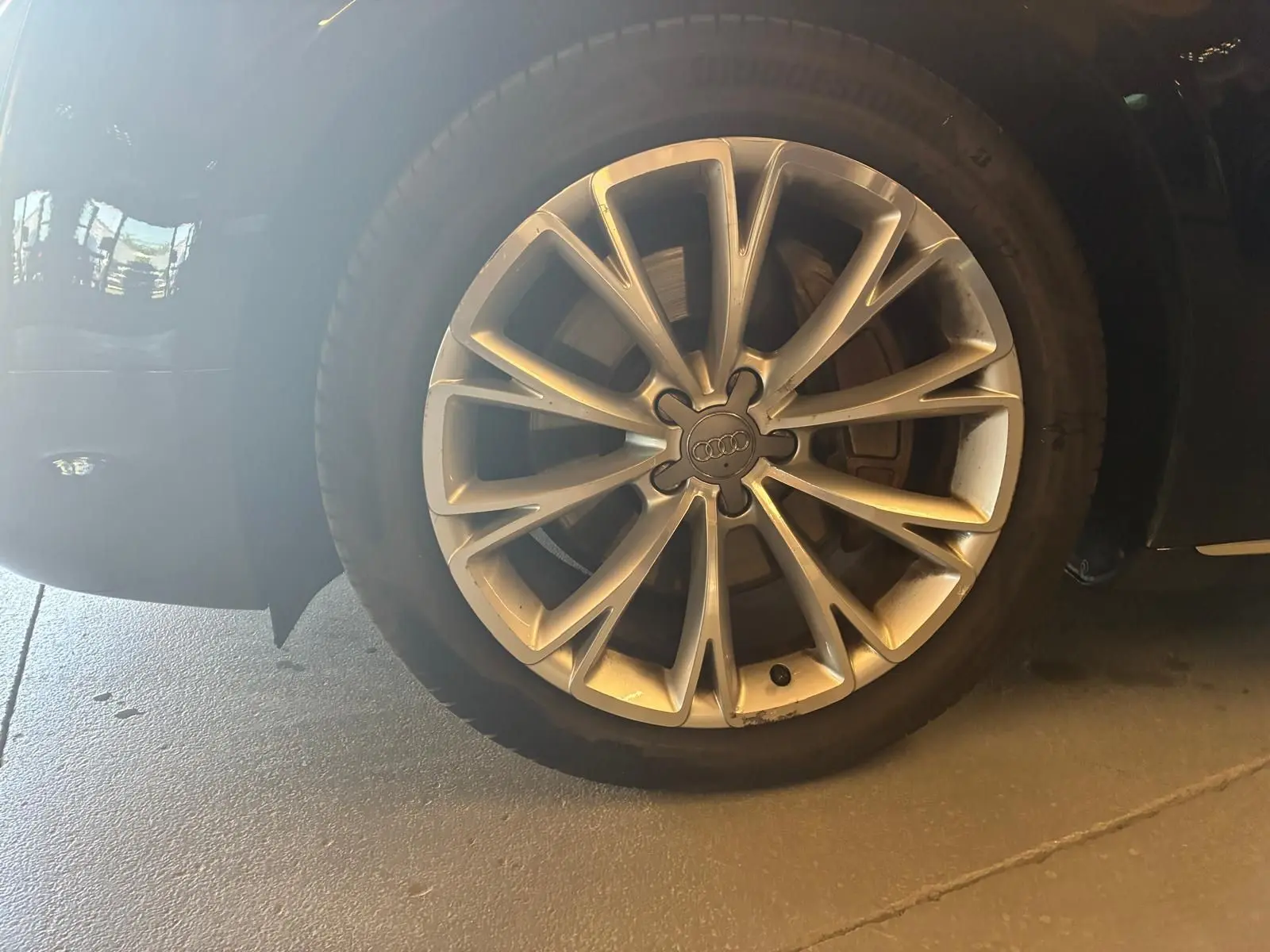 Gros plan sur la roue avant droite d’une Audi A8 noire 2016, mettant en valeur la jante en alliage au design complexe.