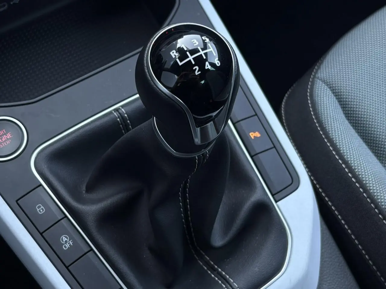 Gros plan sur le levier de vitesses manuel noir avec coutures blanches dans l'habitacle de la SEAT Ibiza gris magnétique.