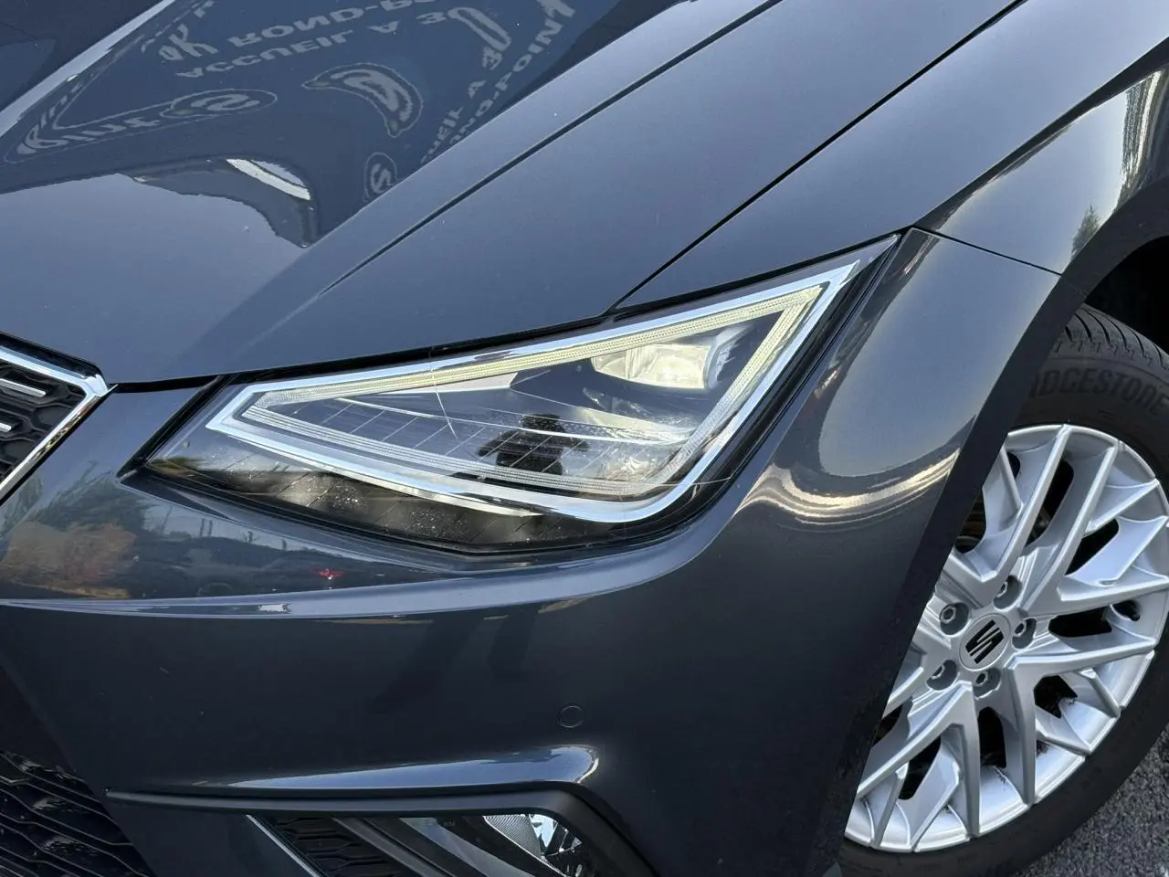 Gros plan sur l'avant droit gris magnétique d'une SEAT Ibiza TSI 115 Xcellence, mettant en valeur le phare et la jante alliage.