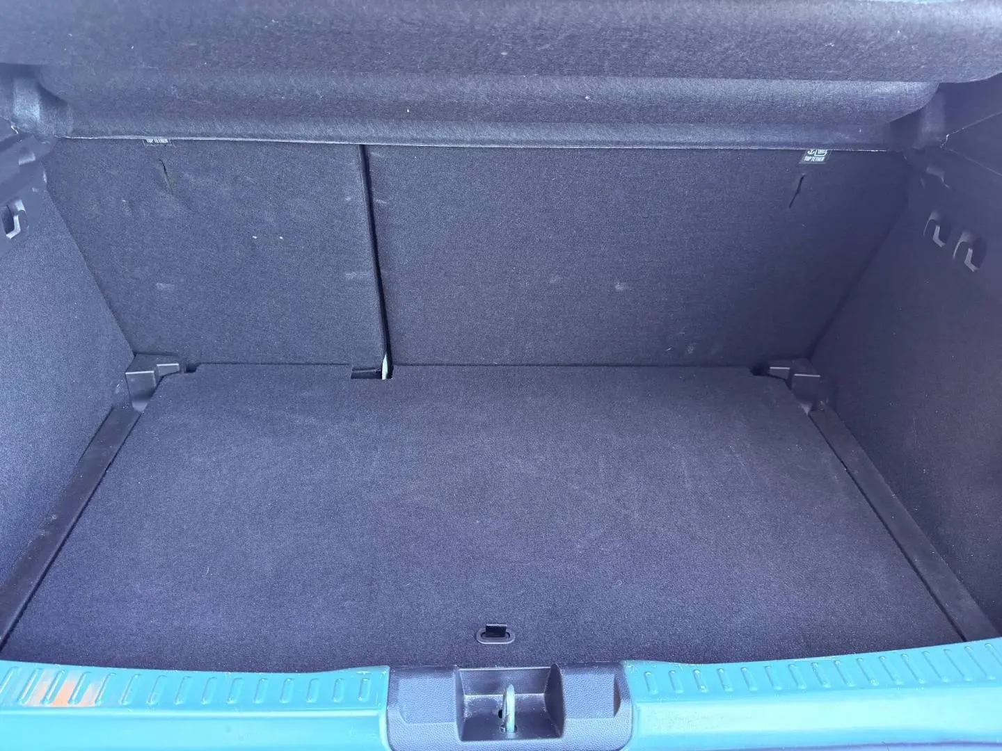 Coffre ouvert d'une Dacia Sandero 2025, vue intérieure, revêtement noir et seuil de coffre vert cèdre métallisé visible.