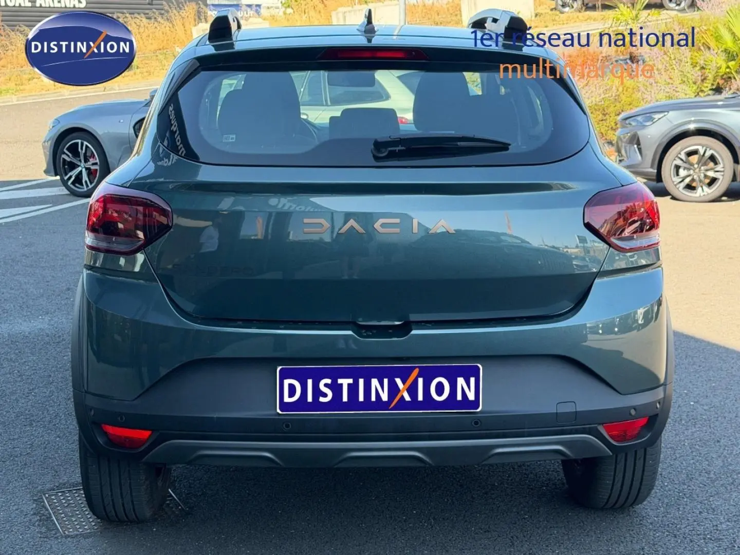 Vue arrière d'une Dacia Sandero 2025 vert cèdre métallisé avec barres de toit et feux arrière rouges.