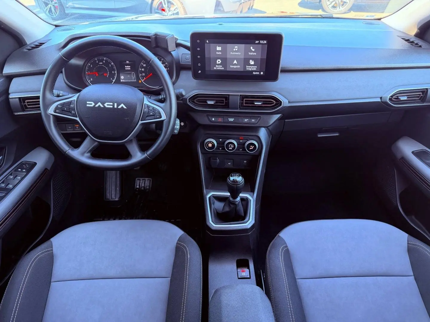 Vue intérieure avant du tableau de bord et volant de la Dacia Sandero 2025 avec écran tactile et boîte manuelle.