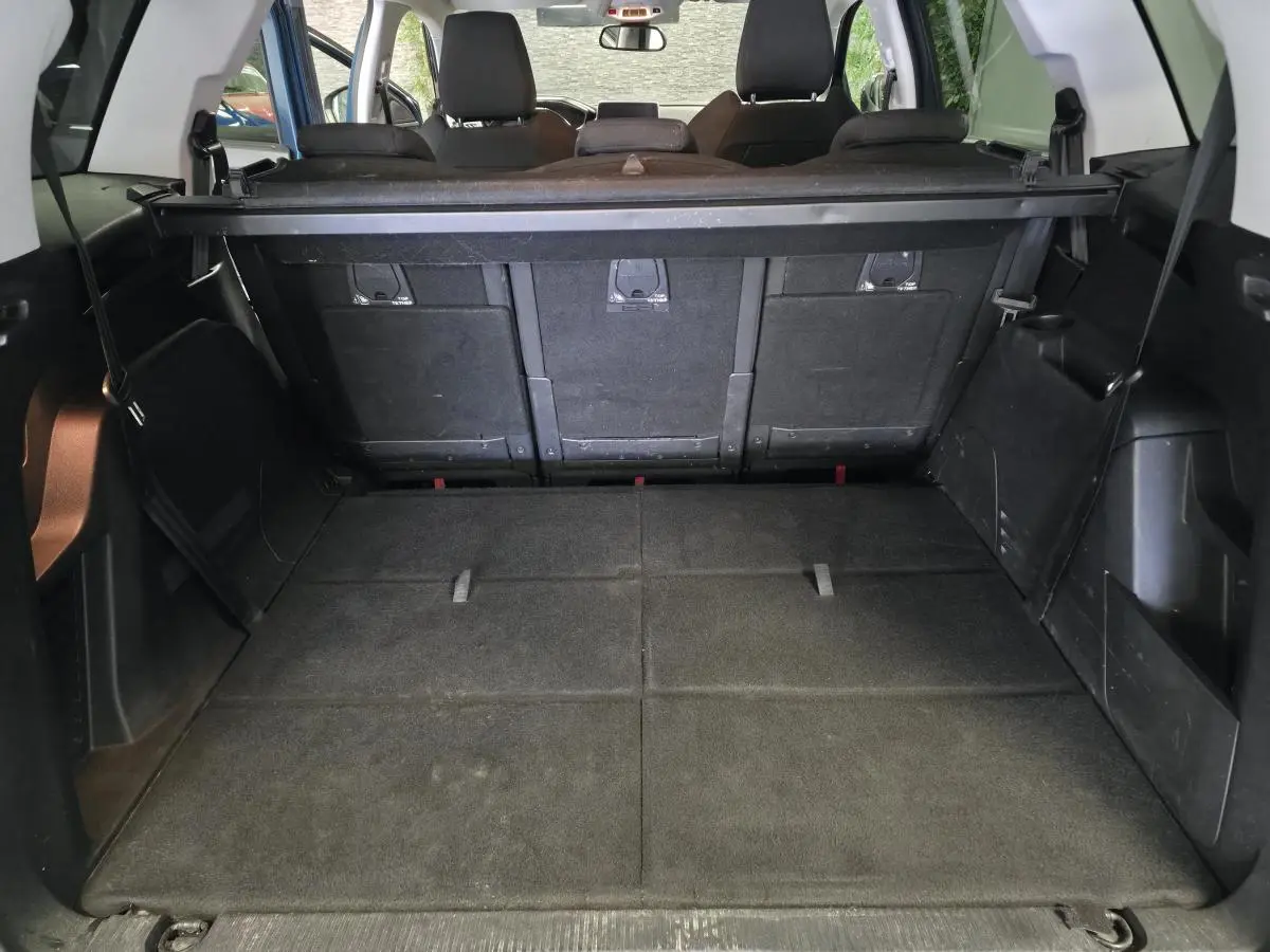 Coffre spacieux du Peugeot 5008 bleu vu de l'arrière avec sièges arrière relevés et cache-bagages noir.
