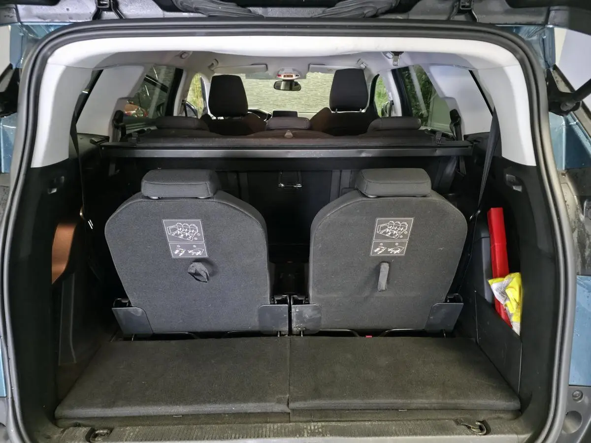 Vue arrière du coffre ouvert d'un Peugeot 5008 bleu 2019, montrant les sièges escamotés du troisième rang et un triangle de sécurité.