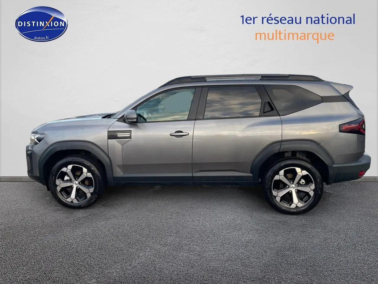 Vue de profil droit du SUV Dacia Bigster gris schiste avec jantes alliage diamantées et barres de toit noires.