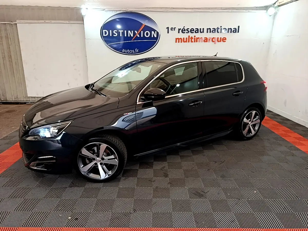 Peugeot 308 gris foncé vue de profil droit en intérieur, avec jantes alliage et phares allumés.