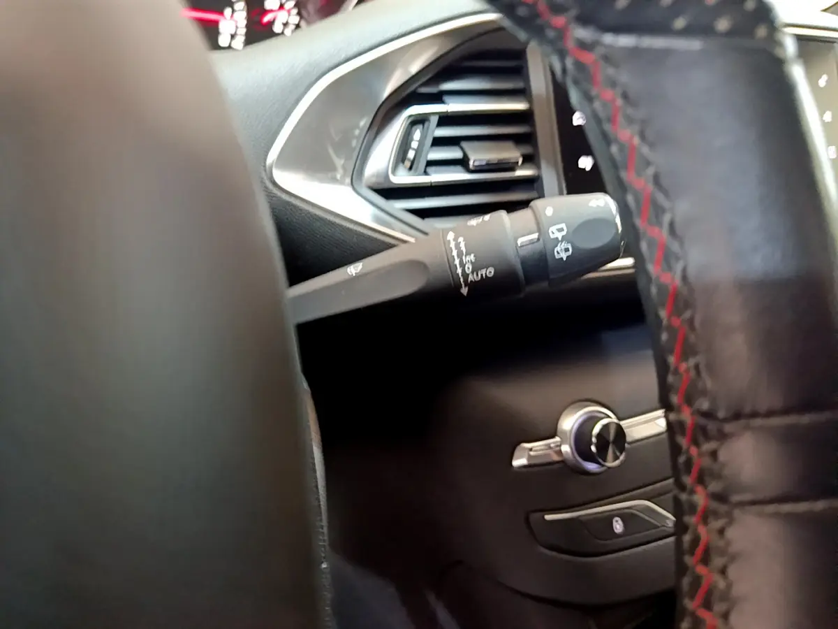 Détail intérieur côté gauche du volant cuir avec commandes d’essuie-glace et aérateur argenté d’une Peugeot 308 gris foncé.