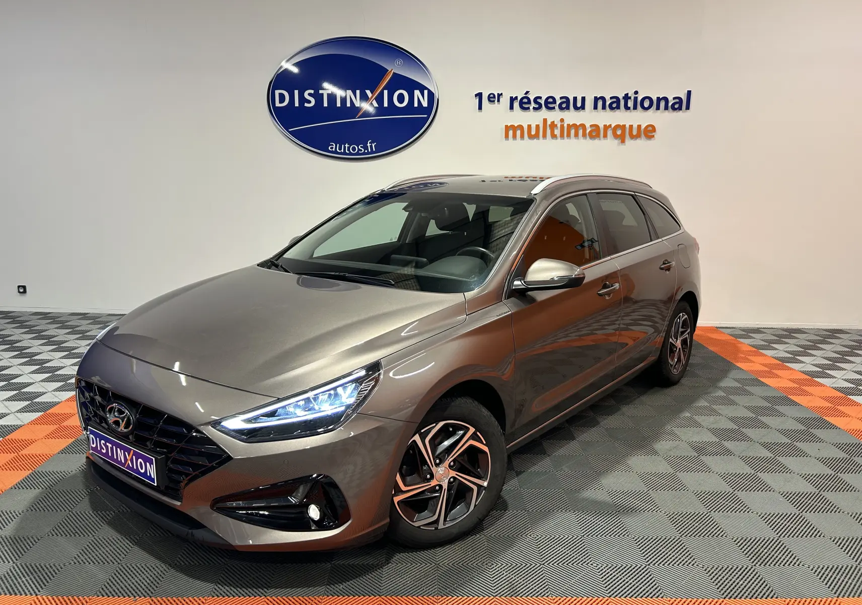 Vue 3/4 avant droit d'une Hyundai i30 SW 2022 couleur bronze métallique avec phares LED allumés en showroom.