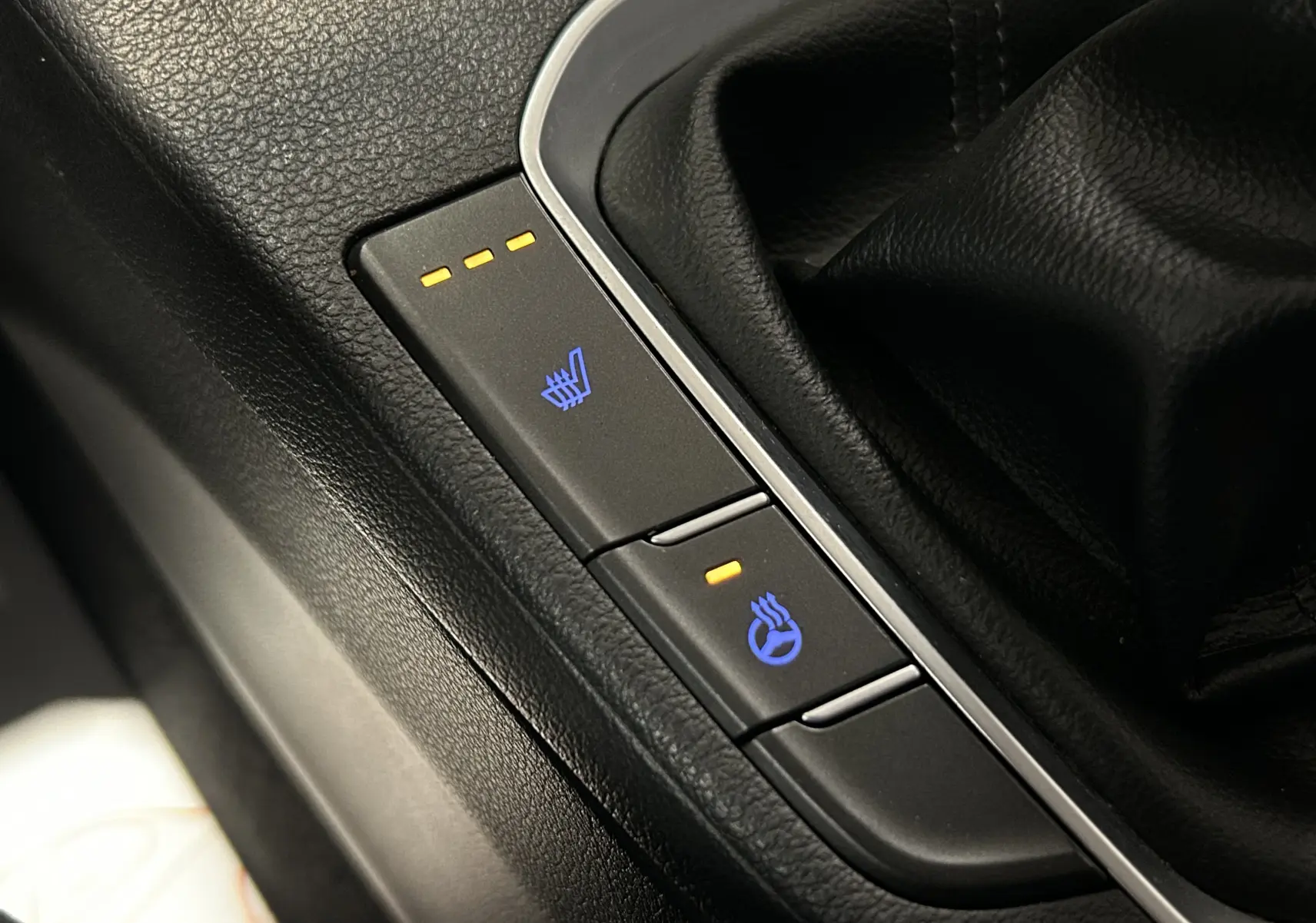 Gros plan sur les boutons de sièges et volant chauffants dans l’habitacle noir de la Hyundai i30 SW 2022.