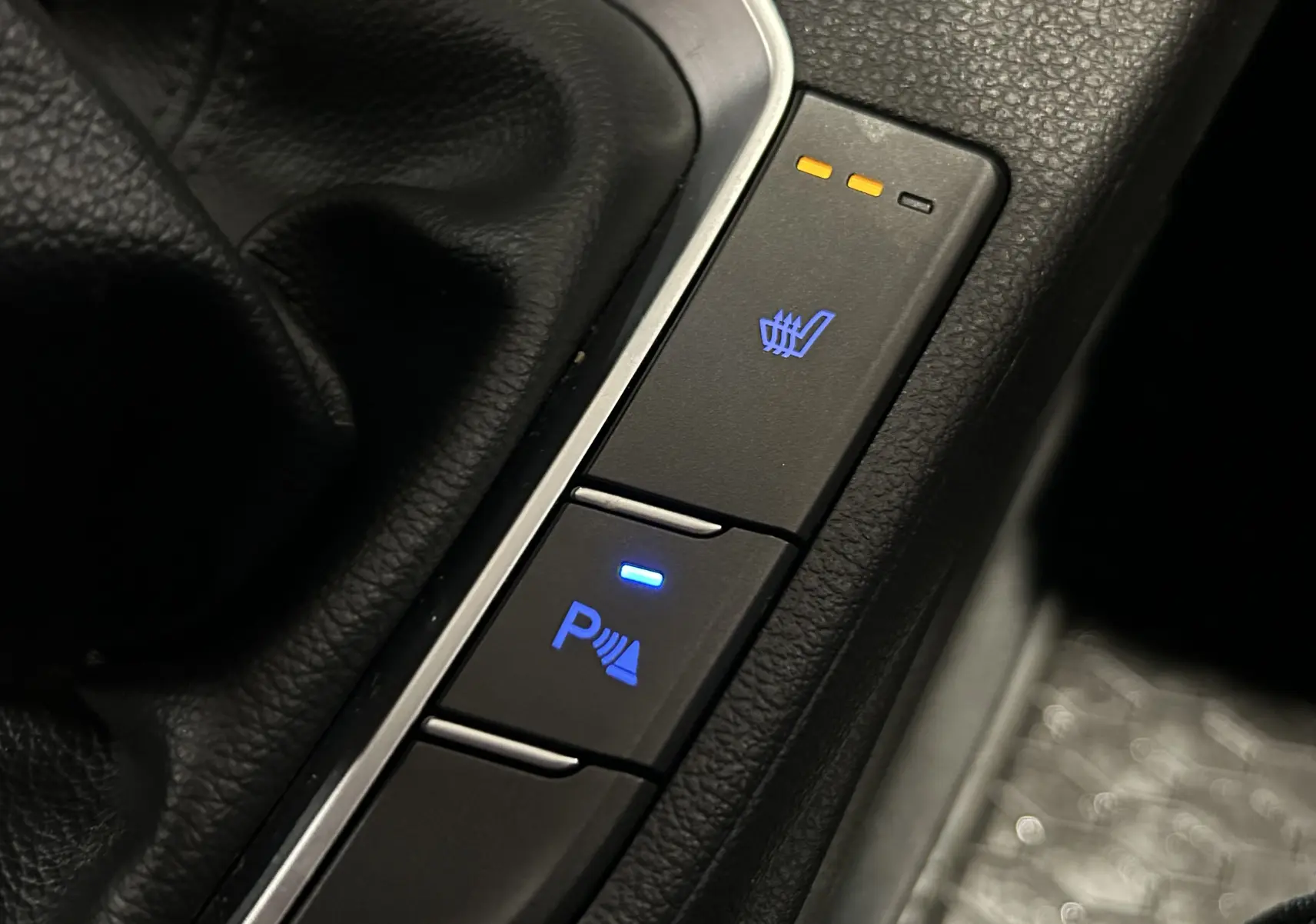 Gros plan sur les boutons de sièges chauffants et assistance parking dans l'habitacle noir de la Hyundai i30 SW 2022.