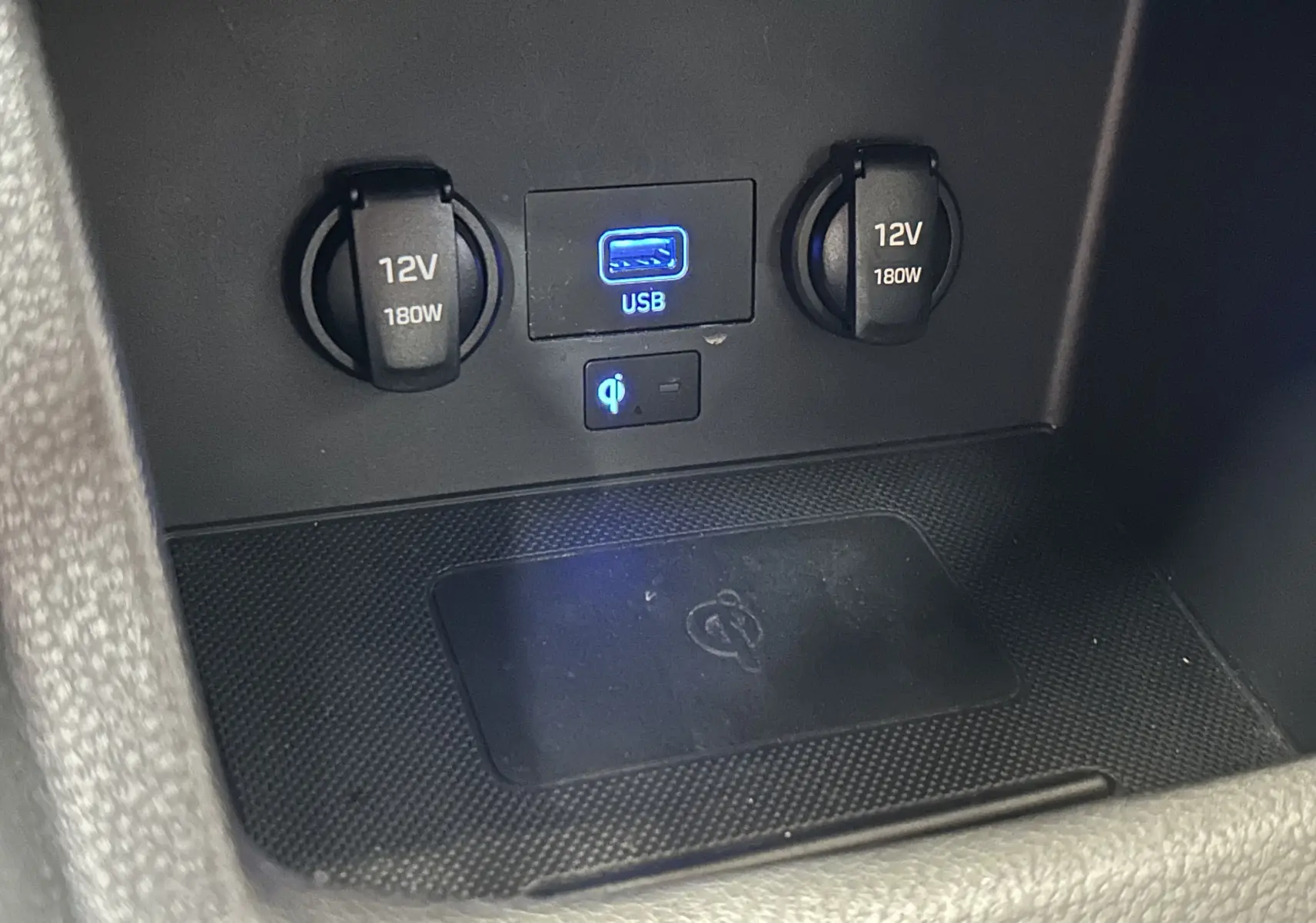 Gros plan sur la console centrale avec prises 12V, port USB bleu et zone de charge sans fil dans une Hyundai i30 SW bronze.