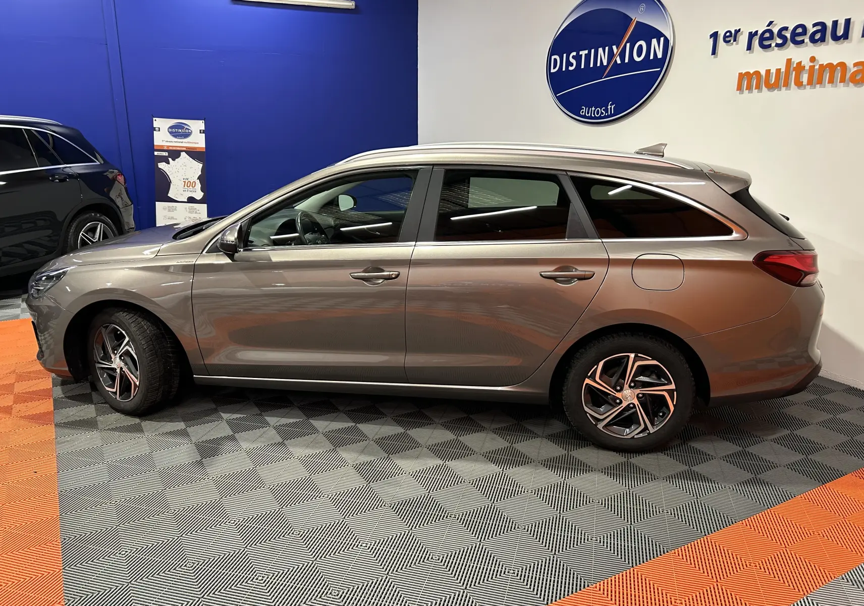 Vue latérale droite d'une Hyundai i30 SW 2022 couleur bronze métallique, avec jantes alliage et vitres teintées, en intérieur showroom.
