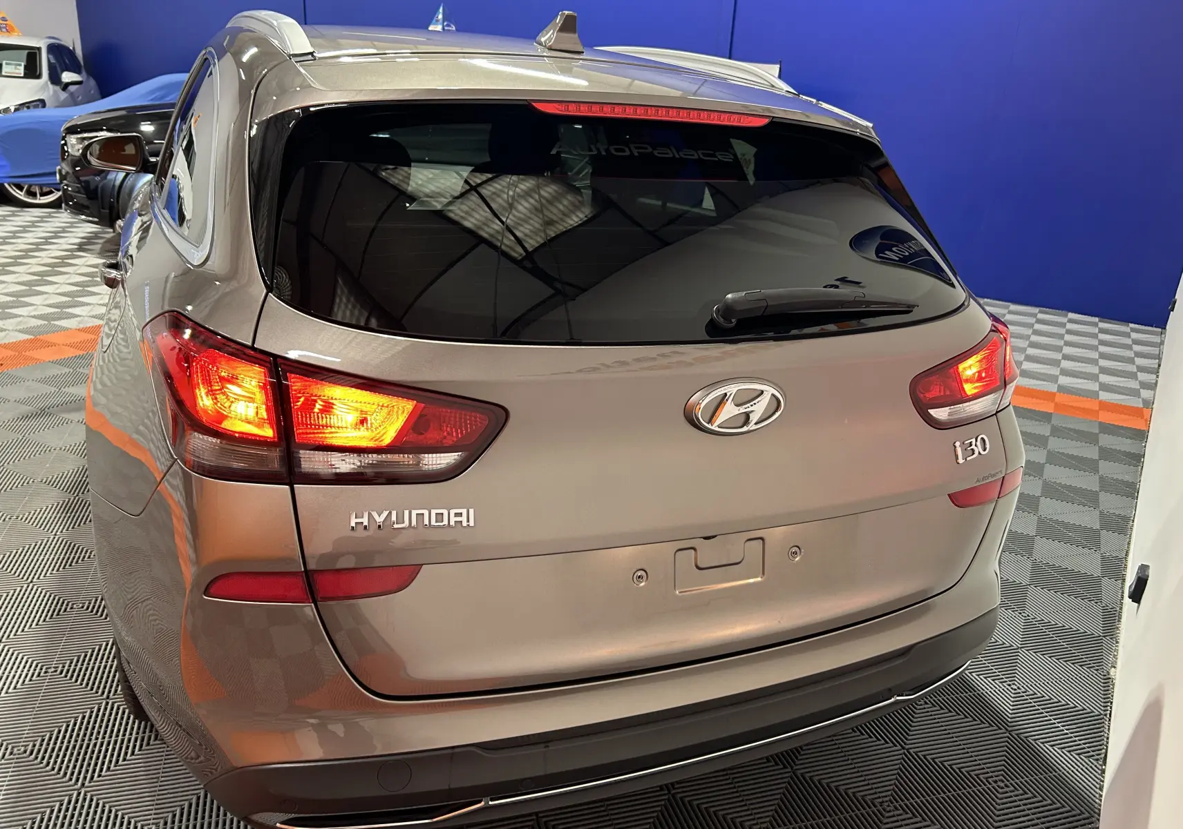 Vue 3/4 arrière gauche d'une Hyundai i30 SW 2022 couleur bronze métallique avec feux arrière allumés en intérieur showroom.