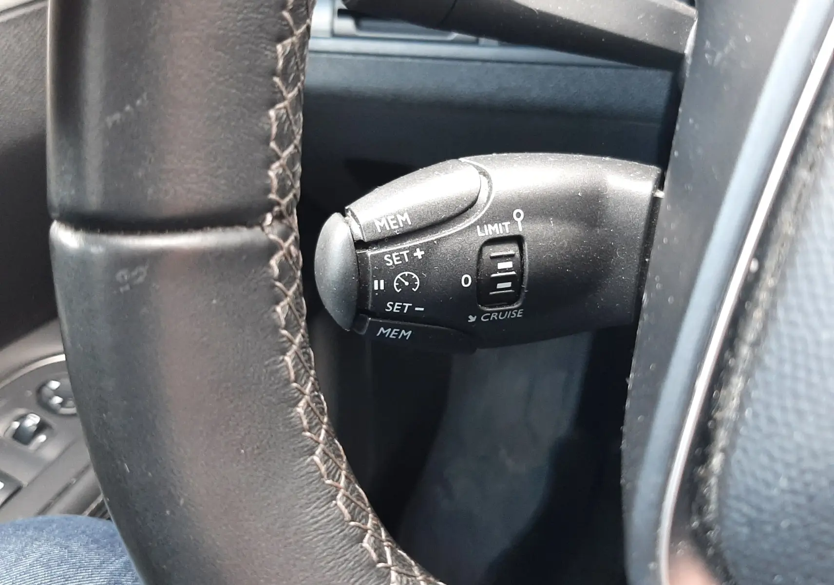 Gros plan sur la commande de régulateur de vitesse à gauche du volant en cuir noir du Peugeot 3008 gris Amazonite.