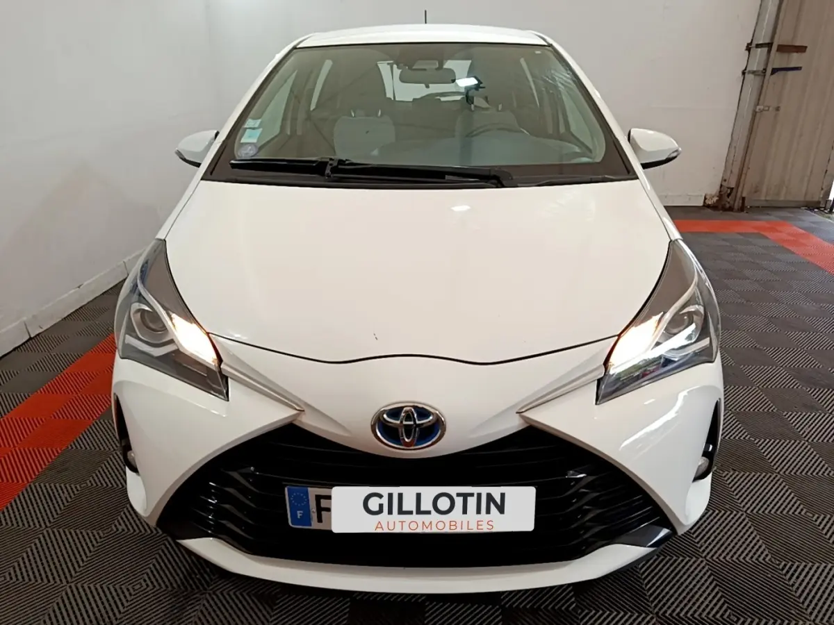 Vue avant d'une Toyota Yaris blanche de 2019 avec phares allumés et calandre noire distinctive.
