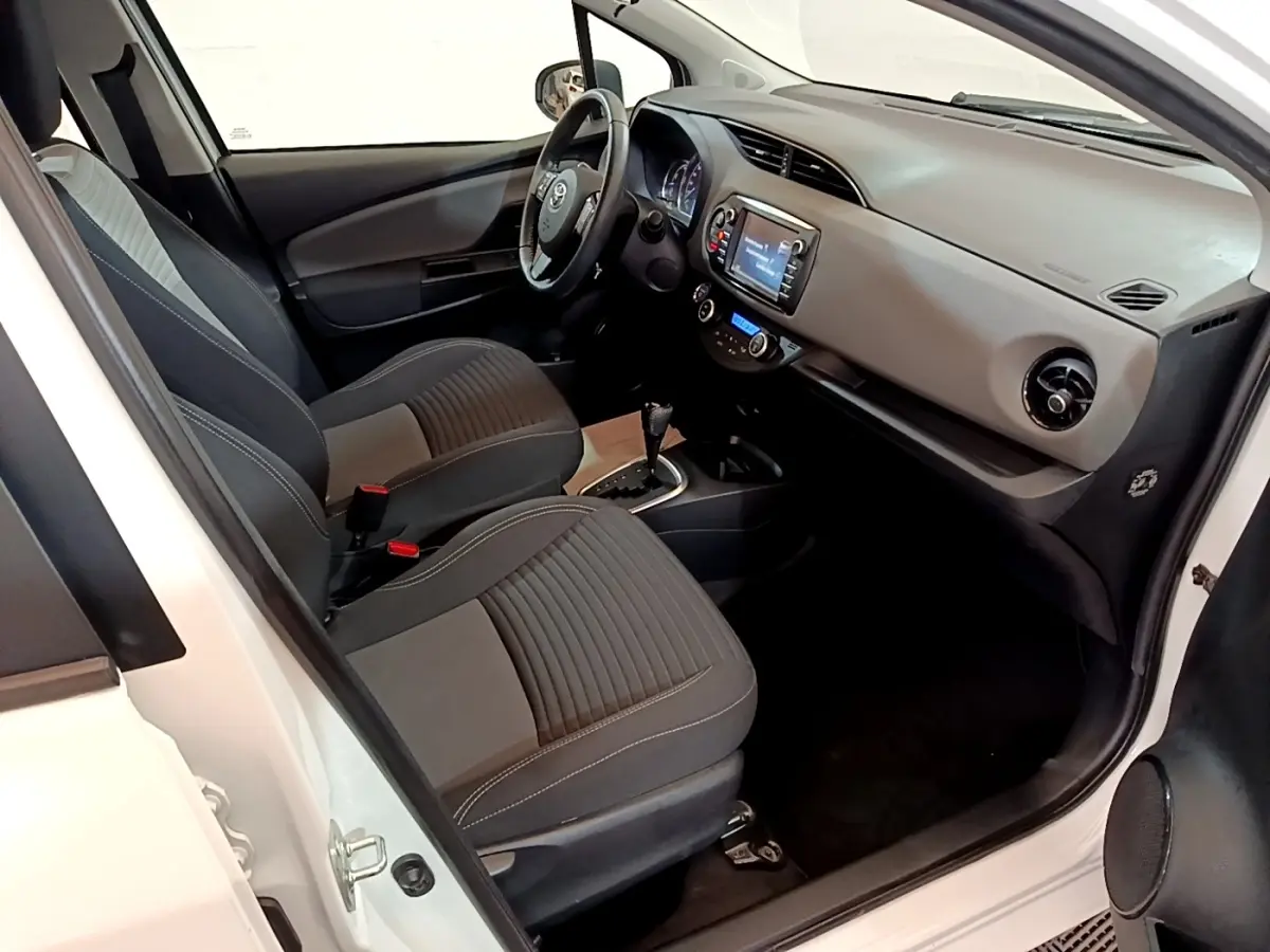 Intérieur avant droit d’une Toyota Yaris blanche 2019, montrant sièges noirs, volant multifonctions et tableau de bord avec écran tactile.