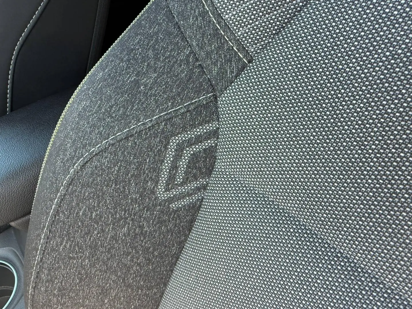Gros plan sur le tissu gris du siège avant droit du Renault Captur 2025 avec logo embossé et surpiqûres claires.