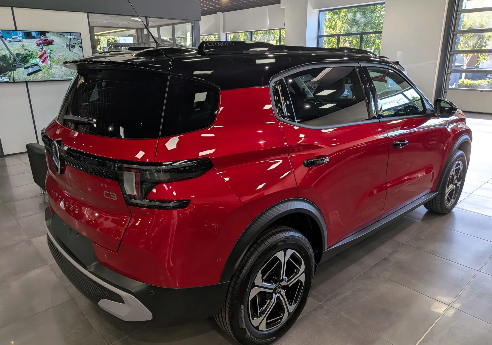 Vue 3/4 arrière droite d'un Citroën C3 Aircross 2026 rouge Elixir avec toit noir, en intérieur showroom.