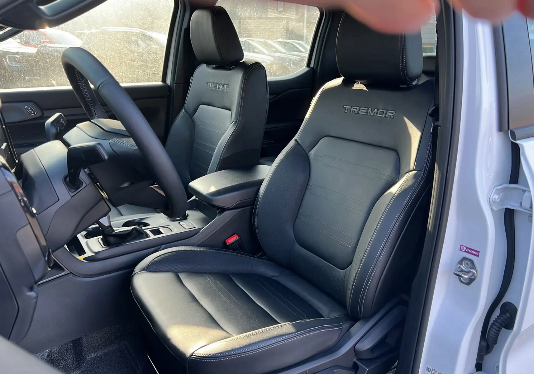 Vue intérieure côté conducteur du Ford Ranger 2025 blanc glacier, sièges noirs avec logo Tremor brodé sur les appuie-têtes.