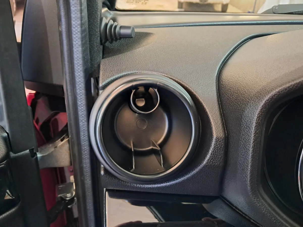 Gros plan sur la sortie d'aération ronde côté conducteur du tableau de bord noir d'une Aixam Ambition rouge.