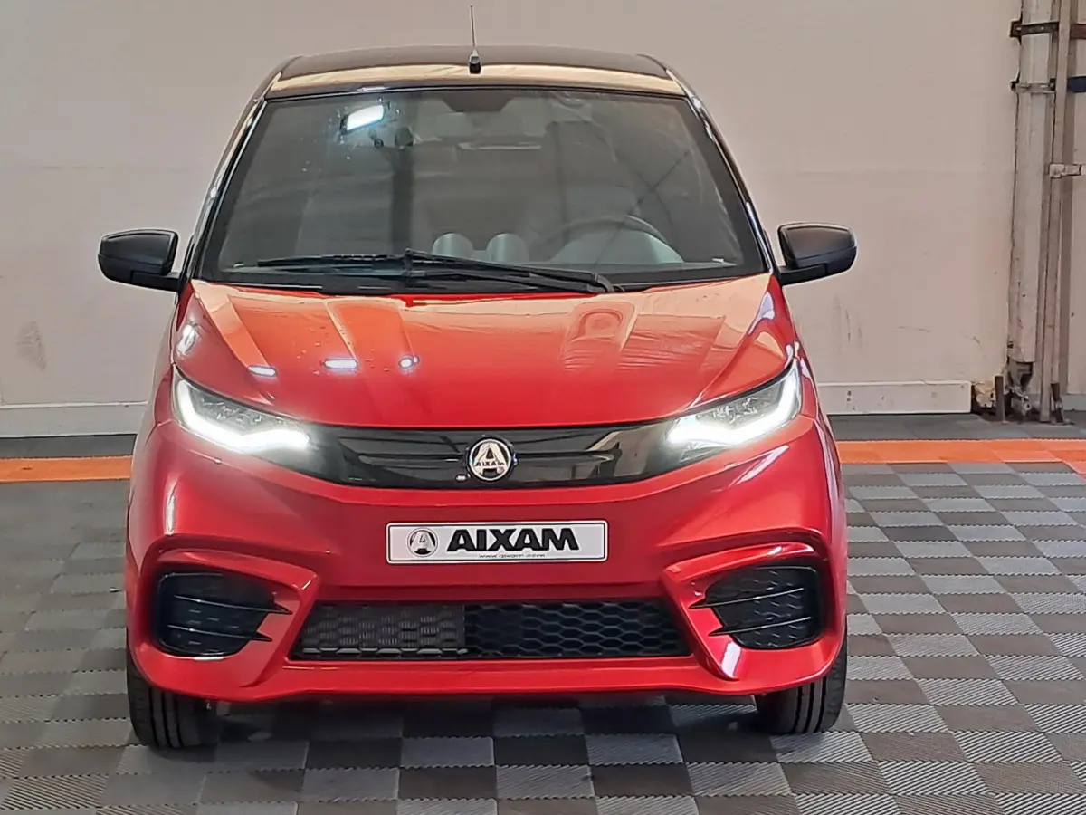 Vue frontale d'une Aixam Ambition rouge 2025 avec phares allumés et calandre noire sportive.