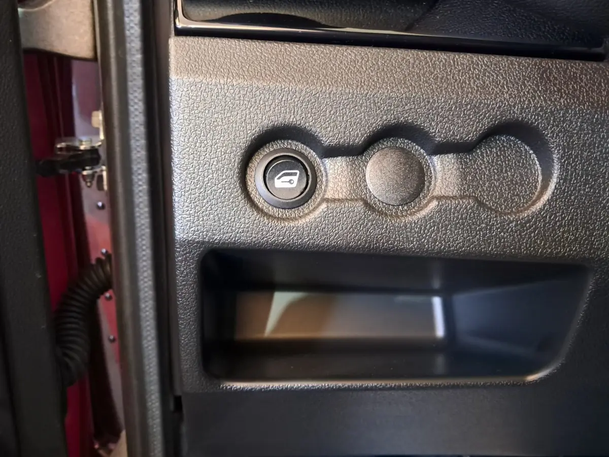 Bouton d'ouverture du coffre sur la portière côté conducteur d'une Aixam Ambition rouge vue de près.