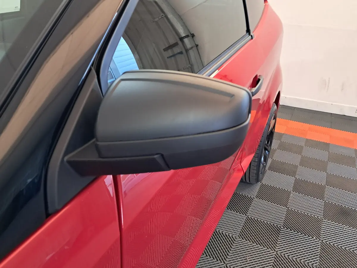 Rétroviseur côté conducteur en gros plan sur la portière rouge d'une Aixam Ambition 2025 stationnée intérieurement.