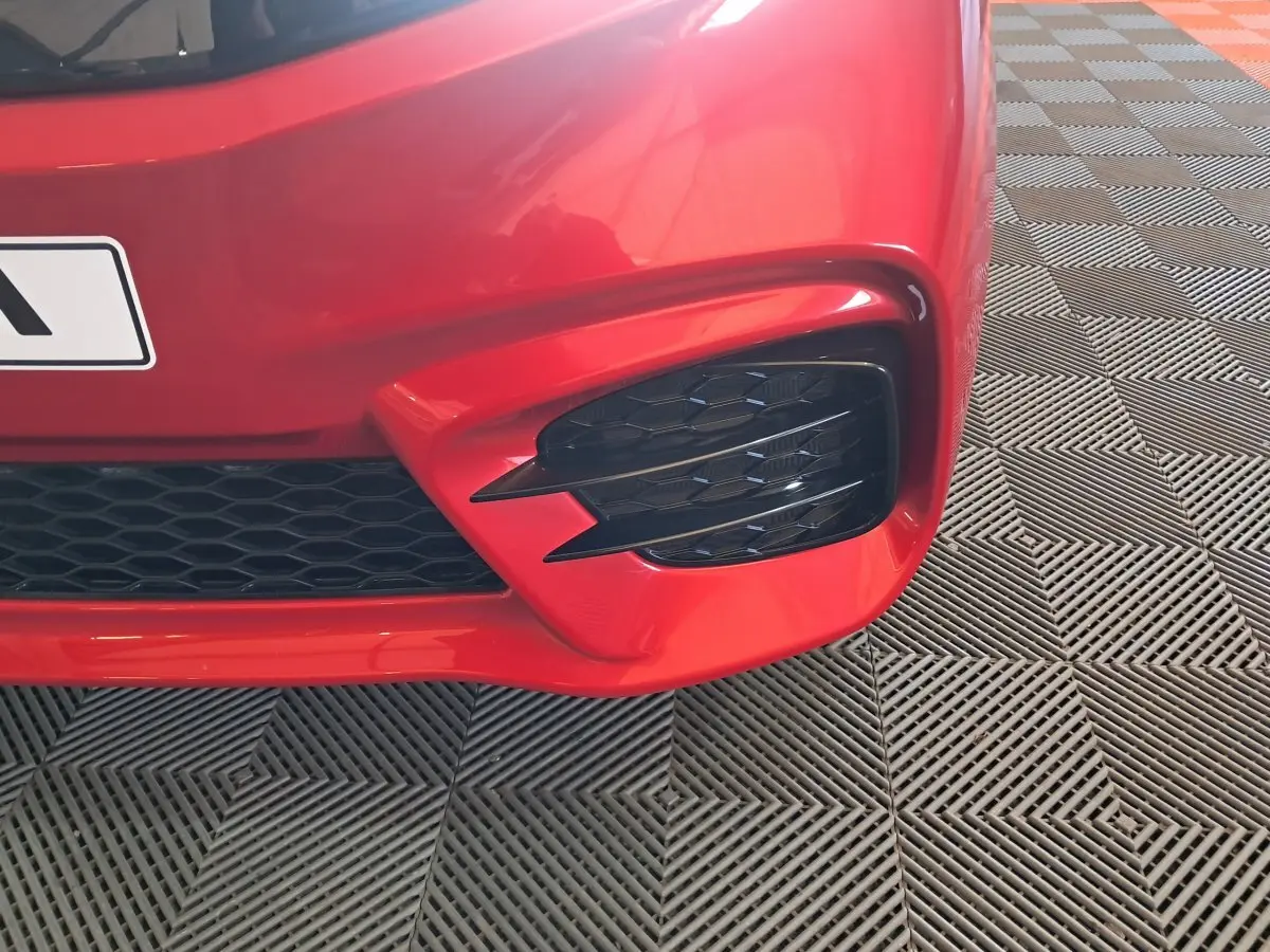 Gros plan sur l'angle avant droit rouge de l'AIXAM AMBITION 2025 avec une grille noire et un éclairage distinctif.