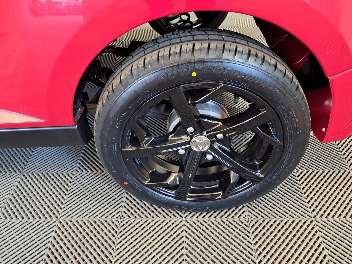 Gros plan sur la roue arrière droite noire brillante d'une AIXAM Ambition rouge 2025 avec jante sport cinq branches.